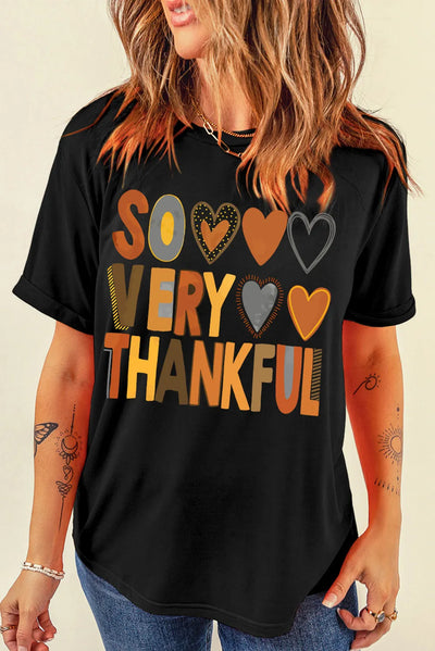 Woman wearing black short sleeve T-shirt with "So Very Thankful" letter graphic, paired with jeans.