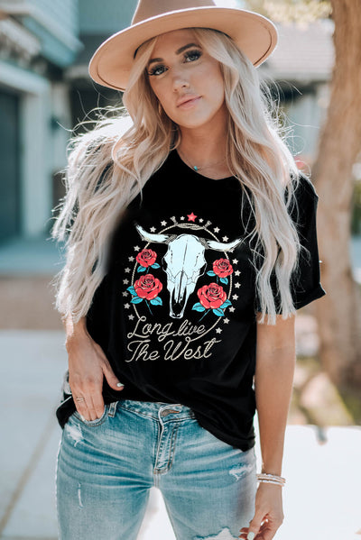 Woman wearing graphic round neck short sleeve t-shirt with skull and roses design, paired with jeans and a hat, outdoors.